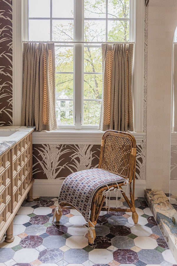 Bathroom with patterned wallpaper, window, and wicker chair.